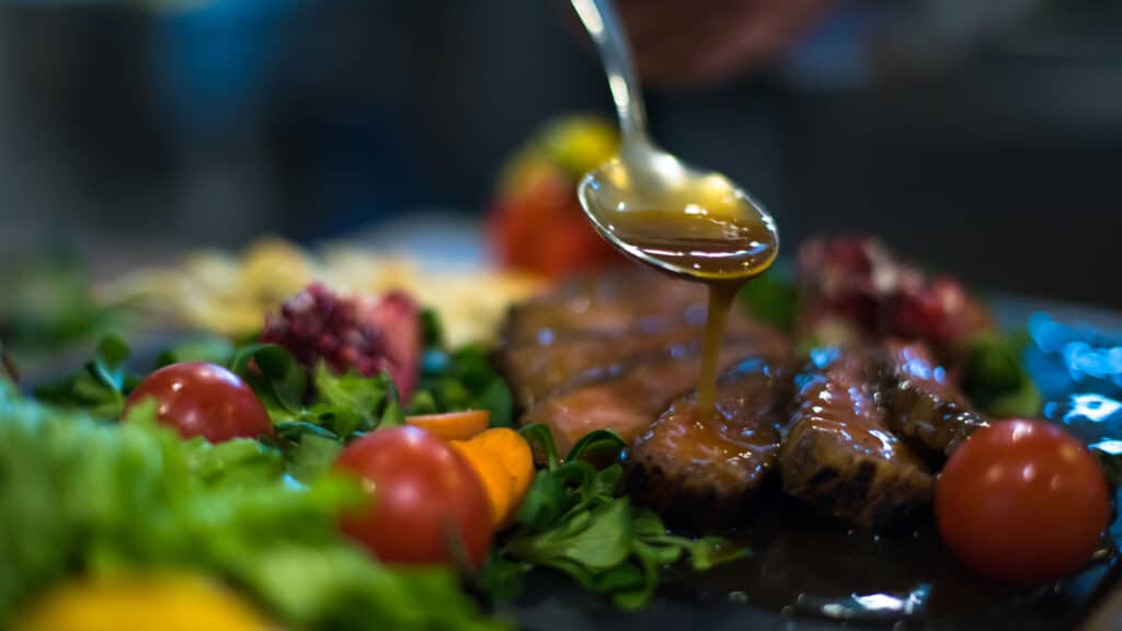 Pouring sauce on gourmet meat dish with vegetables