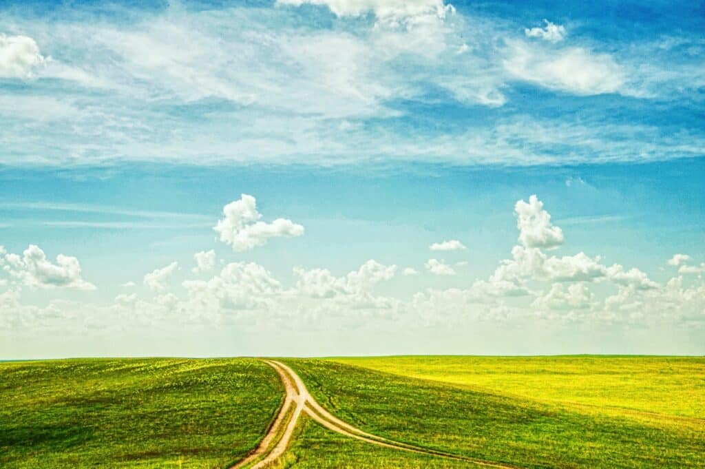 Dirt road through green field under blue sky